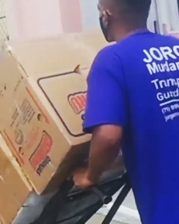 Funcionário de farda azul empurrando caixas num carrinho