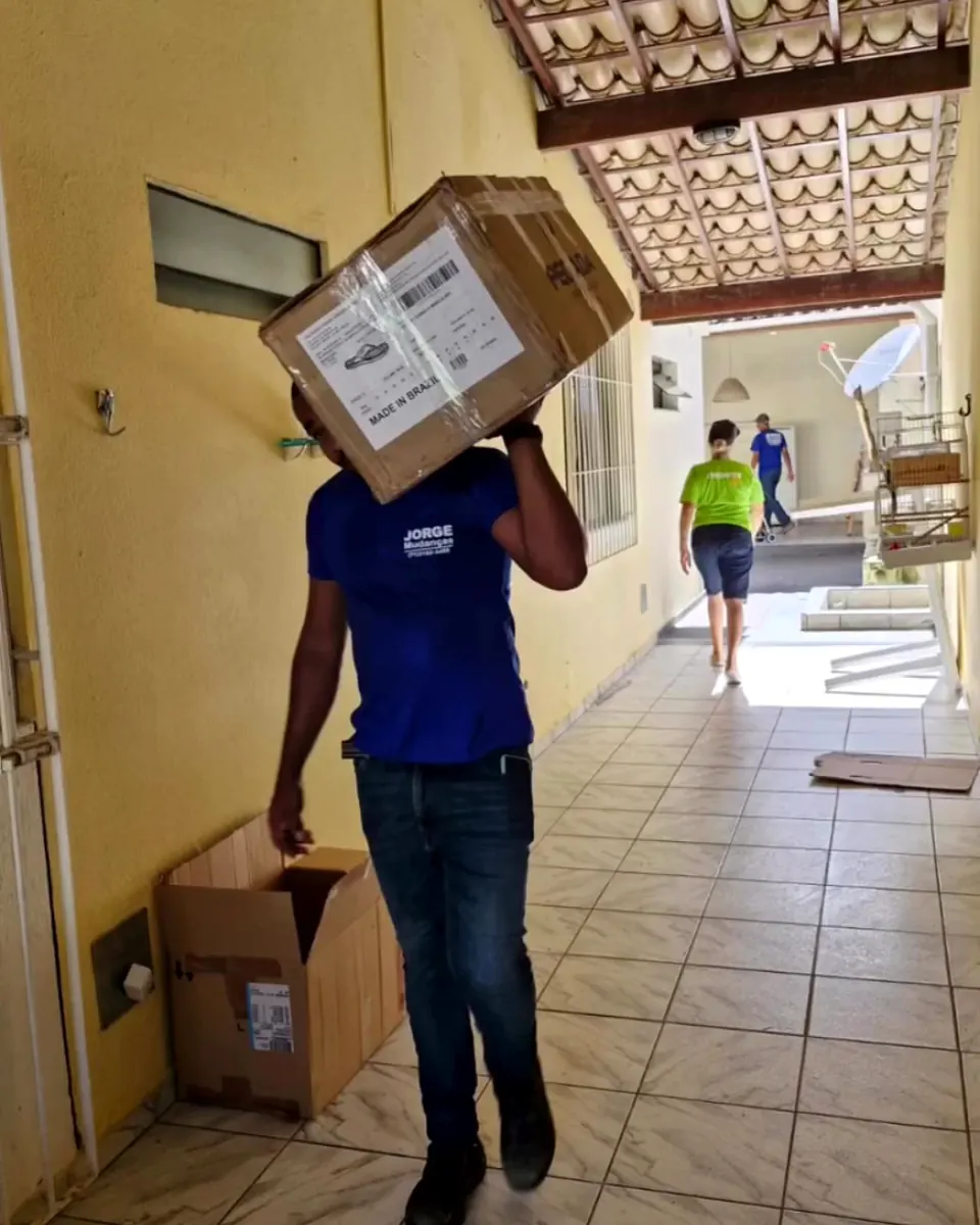Homem da equipe de farda azul carregando uma caixa no ombro por um corredor